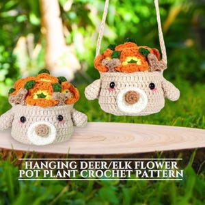 May include: Two crocheted hanging deer or elk planter pots with orange and green flower accents. The pots are beige with a white face and brown eyes. The text "HANGING DEER/ELK FLOWER POT PLANT CROCHET PATTERN" is at the bottom of the image.