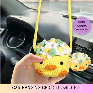 May include: A crocheted yellow chick flower pot with a white and green flower arrangement. The pot is hanging from a yellow string and is being held by a hand. The text "CROCHETTA BY SARA DIGITAL DOWNLOAD PATTERN PDF MADE WITH LOVE" is in a pink circle in the upper right corner of the image. The text "CAR HANGING CHICK FLOWER POT" is at the bottom of the image.