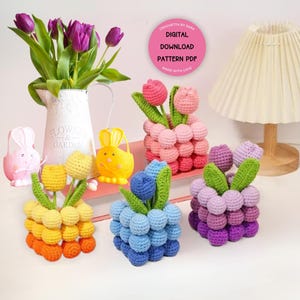May include: A collection of handmade crochet tulip flower arrangements in various colors, including orange, yellow, pink, blue, and purple. The image also features a white pitcher with purple tulips and decorative bunny figurines.