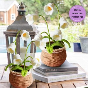 May include: Two crocheted lily of the valley plants in brown pots. The white flowers have yellow centres and green stems and leaves. The pots have a decorative trim. The plants sit on books with the text "STABLES" and "ENGLISH COTTAGE GARDENING". A purple circle with text is in the background.
