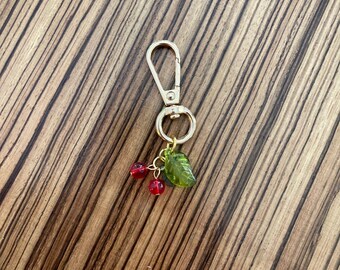 May include: Gold keychain with a green leaf charm and two red bead cherries.