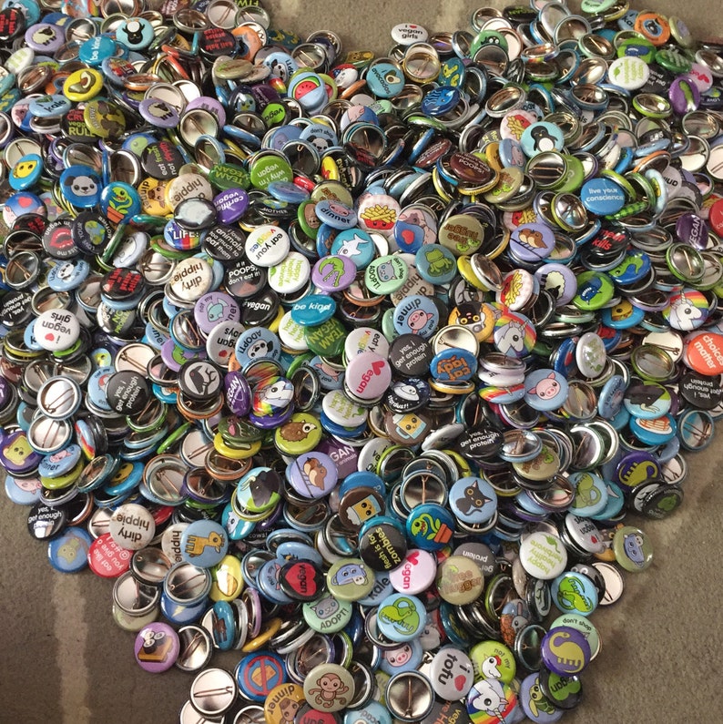 May include: A large collection of colorful round buttons with various designs and messages. The buttons feature a variety of themes, including animals, food, and inspirational quotes.