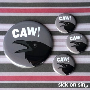 May include: Four grey and black round buttons with a black crow and the word "CAW!" in white text. The buttons are on a striped background.