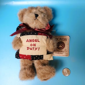 Peut inclure: Un ours en peluche brun avec un ruban rouge et un gilet patchwork avec l'inscription "ANGEL ON DUTY!". L'ours porte une &eacute;tiquette de "BOYDS The Head Bean Collection". Une pi&egrave;ce de monnaie am&eacute;ricaine est &agrave; c&ocirc;t&eacute; de l'ours.