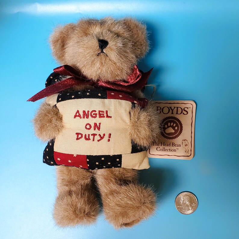 Peut inclure: Un ours en peluche brun avec un ruban rouge et un gilet patchwork avec l'inscription "ANGEL ON DUTY!". L'ours porte une &eacute;tiquette de "BOYDS The Head Bean Collection". Une pi&egrave;ce de monnaie am&eacute;ricaine est &agrave; c&ocirc;t&eacute; de l'ours.