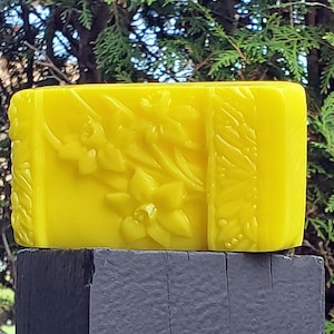 May include: A bright yellow soap bar with a floral design. The soap is rectangular and has a raised design of flowers and leaves.