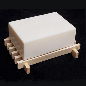 May include: A white bar of soap resting on a wooden soap dish with a natural wood finish.
