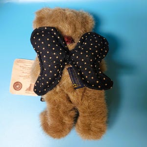 Peut inclure: Un ours en peluche marron avec un n&oelig;ud papillon noir orn&eacute; d'&eacute;toiles dor&eacute;es. L'ours a une &eacute;tiquette attach&eacute;e. Le n&oelig;ud papillon est en tissu doux. L'ours est un objet de collection.