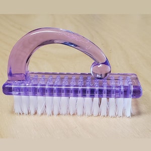 May include: A purple plastic nail brush with a curved handle and white bristles.
