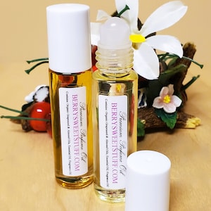 Könnte beinhalten: Zwei transparente Glas-Rollflaschen mit weißen Kappen und Etiketten. Die Etiketten sind weiß mit rosa Schrift, auf der "Premium Perfume Oil" und "BERRYSWEETSTUFF.COM" steht. Die Flaschen stehen auf einer Holzoberfläche.