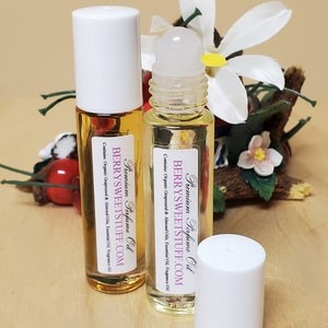 Könnte beinhalten: Zwei transparente Glas-Rollflaschen mit weißen Kappen und Etiketten mit der Aufschrift "Premium Perfume Oil" und "BERRYSWEETSTUFF.COM". Die Flaschen enthalten eine hellgelbe Flüssigkeit und stehen auf einer Holzoberfläche.
