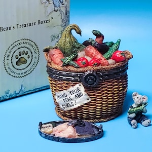 May include: A decorative basket-shaped trinket box filled with miniature vegetables, including carrots, tomatoes, and peas. The box has a hinged lid and a small sign that reads "MIND YOUR PEAS AND CUKES!". A small bear figurine is nearby.