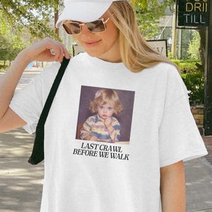 May include: White t-shirt with a vintage photo print and the text "LAST CRAWL BEFORE WE WALK". The shirt is a casual style, suitable for everyday wear.
