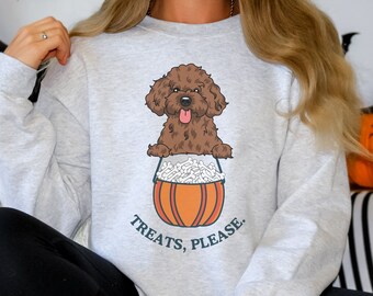 May include: A gray sweatshirt with a brown dog wearing a Halloween costume. The dog is sitting in a pumpkin-shaped bucket filled with bones. The text "Treats, Please." is printed below the dog.