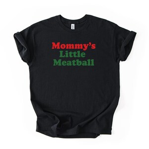 May include: Black t-shirt featuring the text "Mommy's Little Meatball" in red and green. The shirt has a crew neck and is made of a soft fabric. A casual, comfortable item of clothing.