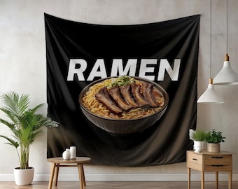 Puede incluir: Tapiz de pared negro con un diseño de cuenco de ramen. La palabra "RAMEN" está impresa en blanco sobre el cuenco de fideos, caldo y carne. El tapiz está colgado en una pared, con una mesa y plantas delante.