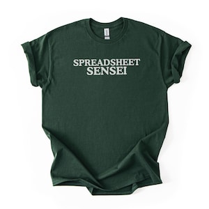 May include: Dark green t-shirt with the text "SPREADSHEET SENSEI" in white block letters. The shirt is folded, showing the rolled-up sleeves. The t-shirt is made of a soft material.