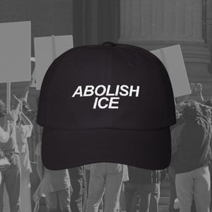 May include: Black baseball cap with white embroidered text "ABOLISH ICE" on the front. The cap is worn by a person in a crowd of people holding signs.