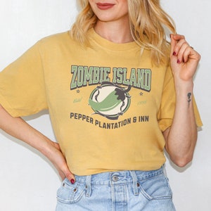 May include: A yellow t-shirt with a green chili pepper graphic and the text "Zombie Island Pepper Plantation & Inn" printed on the front.