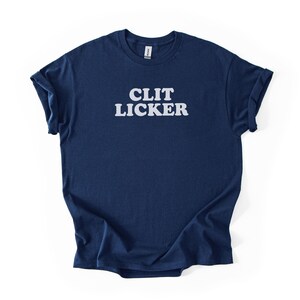 May include: Navy blue t-shirt with the white text "CLIT LICKER" printed across the chest. The shirt has short sleeves and a crew neck. The fabric is soft and appears to be cotton.