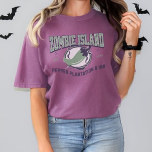 May include: Purple t-shirt with a green chili pepper graphic and the text "Zombie Island Pepper Plantation & Inn Established 1998"