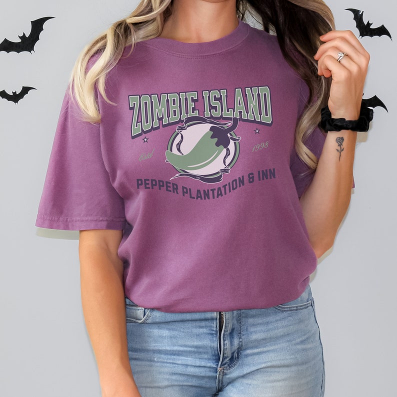 May include: Purple t-shirt with a green chili pepper graphic and the text "Zombie Island Pepper Plantation & Inn Established 1998"