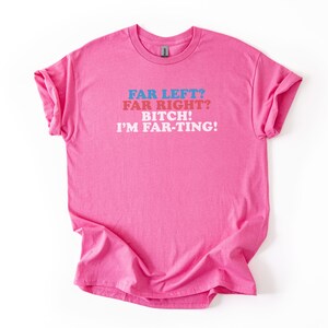 May include: A bright pink t-shirt with rolled-up sleeves. The shirt features the text "FAR LEFT? FAR RIGHT? BITCH! I'M FAR-TING!" in blue, red, and white lettering. The shirt is made of a soft material.