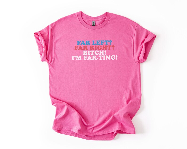 May include: A bright pink t-shirt with rolled-up sleeves. The shirt features the text "FAR LEFT? FAR RIGHT? BITCH! I'M FAR-TING!" in blue, red, and white lettering. The shirt is made of a soft material.