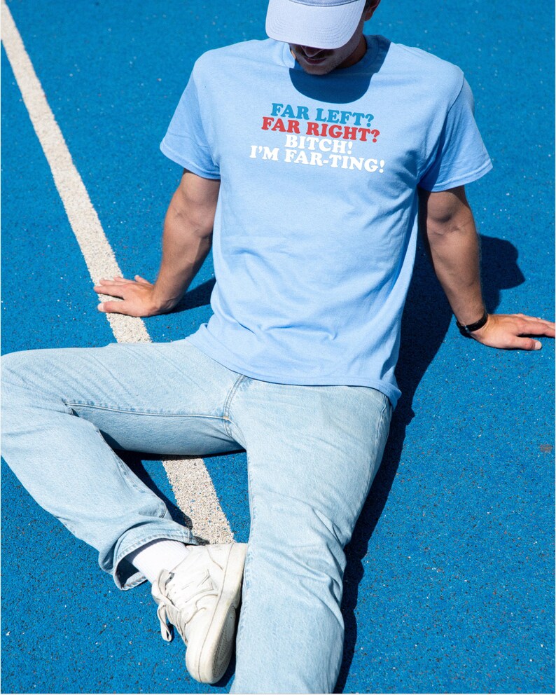 May include: Light blue t-shirt with the text "FAR LEFT? FAR RIGHT? BITCH! I'M FAR-TING!" in red and white. The person is wearing light blue jeans, white sneakers, and a light blue cap. The background is blue.