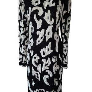 May include: Black dress with long sleeves, adorned with white abstract patterns. The dress features a round neckline and is covered in sequins. The design is a striking contrast of black and white, creating a bold visual statement.