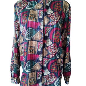 Puede incluir: Una blusa abotonada de manga larga con un colorido estampado abstracto. La blusa presenta una mezcla de colores, incluyendo azul marino, rosa, verde y marrón. El estampado incluye formas geométricas y diseños florales. La blusa se muestra en un maniquí negro.