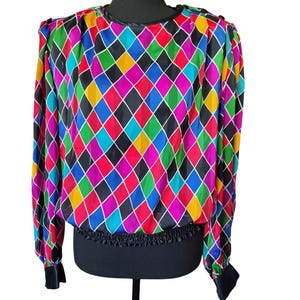 May include: A long-sleeve blouse featuring a vibrant, multi-colored diamond harlequin pattern in shades of red, blue, green, yellow, and black. The garment has a round neckline, gathered shoulders, and a black elasticized waistband and cuffs.