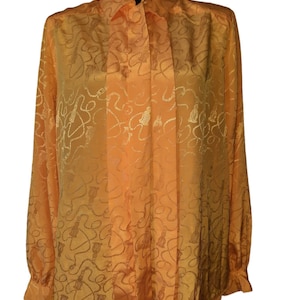 May include: Orange long-sleeve blouse with a bow tie collar. The blouse has a subtle pattern of swirls and tassels. The sleeves have buttoned cuffs. The fabric has a slight sheen.