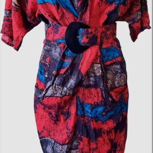 Könnte beinhalten: Vintage-Kleid mit abstraktem Muster in Rot, Blau und Schwarz. Es hat einen V-Ausschnitt, kurze Ärmel und einen schwarzen Gürtel mit großer Schnalle. Der Stoff wirkt leicht.