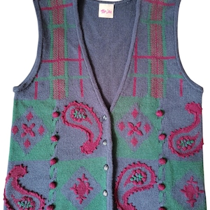 May include: A button-up, V-neck sweater vest in shades of blue, green, and fuchsia. The vest features a plaid pattern on the shoulders and a paisley design on the front. The label reads "Tan Jay".