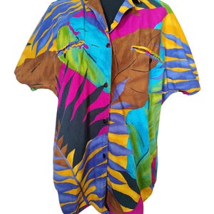 May include: A short-sleeved button-down shirt with a vibrant tropical leaf pattern. The shirt features a mix of colors, including brown, blue, yellow, pink, and green. The shirt is displayed on a black mannequin.
