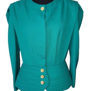 May include: Teal-colored blouse with long sleeves and gold-colored buttons. The blouse features a pleated waist and a round neckline. The buttons are decorative and add a touch of elegance to the garment. The blouse is displayed on a black mannequin.
