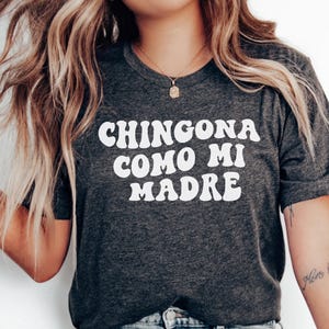 May include: A dark gray t-shirt with the text "CHINGONA COMO MI MADRE" in white, stylized lettering.