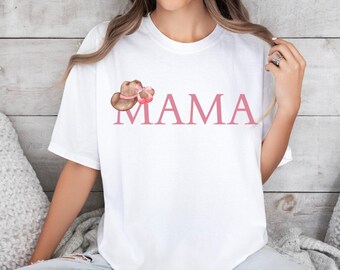 May include: White t-shirt with a pink "MAMA" graphic and a brown cowboy hat with a pink bow.