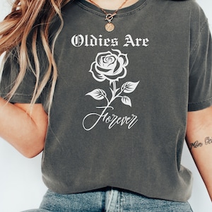 May include: A dark grey t-shirt with a white graphic design featuring a rose and the text "Oldies Are Forever".