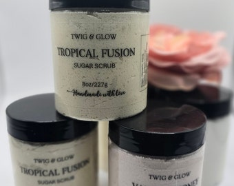 May include: Three jars of sugar scrub with black lids. The jars are labeled "Tropical Fusion Sugar Scrub", "Tropical Fusion Sugar Scrub", and "Vanilla Honey Sugar Scrub". Each jar is 8 oz/227g and says "Handmade with love".