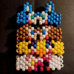 Könnte beinhalten: Ein handgefertigtes Kandi-Armband mit einem mehrschichtigen Design. Die oberste Schicht hat blaue, weiße und rote Perlen, gefolgt von braunen, gelben und rosa Schichten. Das Armband besteht aus Kunststoffperlen, die zusammen aufgefädelt sind.