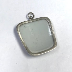 May include: Silver pendant with a square-shaped, white porcelain insert. The pendant has a simple, elegant design.