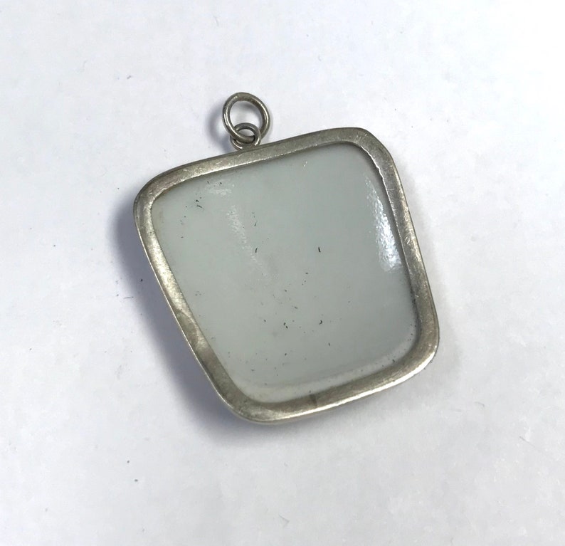 May include: Silver pendant with a square-shaped, white porcelain insert. The pendant has a simple, elegant design.
