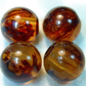 May include: Four round beads with a marbled pattern in shades of brown, amber, and red. Each bead has a glossy finish and a hole drilled through the center, suggesting they are for jewelry making or crafts.
