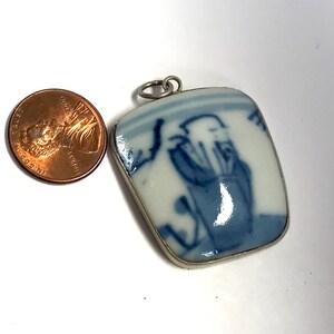 May include: A blue and white porcelain pendant with a silver bail. The pendant features a hand-painted design of a person in a blue robe.