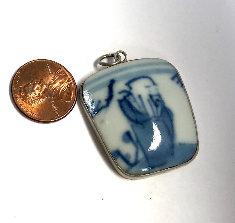 May include: A blue and white porcelain pendant with a silver bail. The pendant features a hand-painted design of a person in a blue robe.