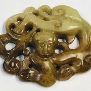May include: A jade carving of a monkey holding onto a branch with intricate details. The carving is a light green color with brown accents.