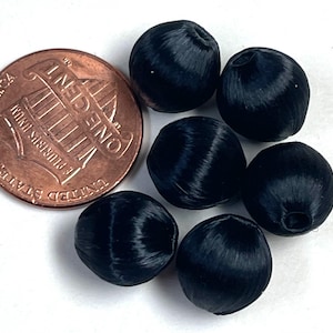 May include: Close-up of six black satin beads with a penny for size comparison. The beads are round with a slight oval shape and have a textured, woven appearance. The penny shows the profile of Abraham Lincoln.