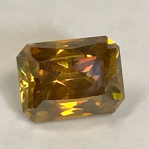 May include: A large, emerald-cut gemstone with a golden-brown hue. The stone has a faceted cut and is highly reflective.